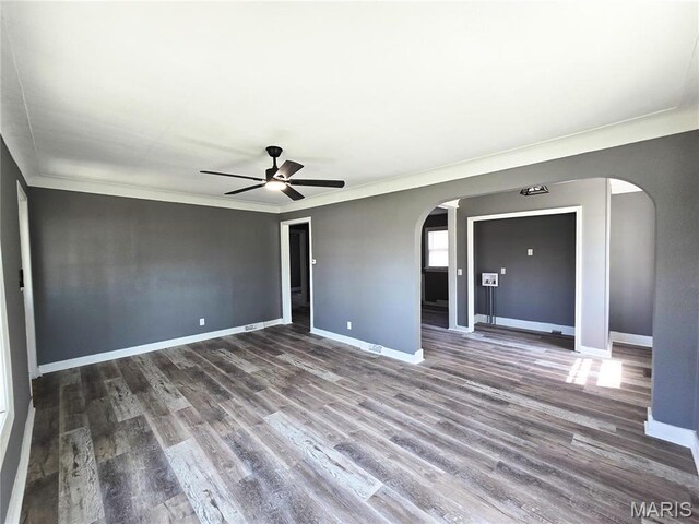 spare room with arched walkways, baseboards, wood finished floors, ceiling fan, and ornamental molding