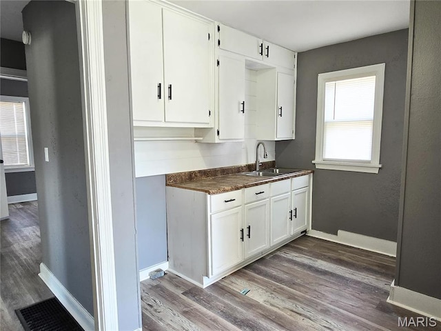 kitchen featuring a sink, wood finished floors, dark countertops, white cabinets, and baseboards
