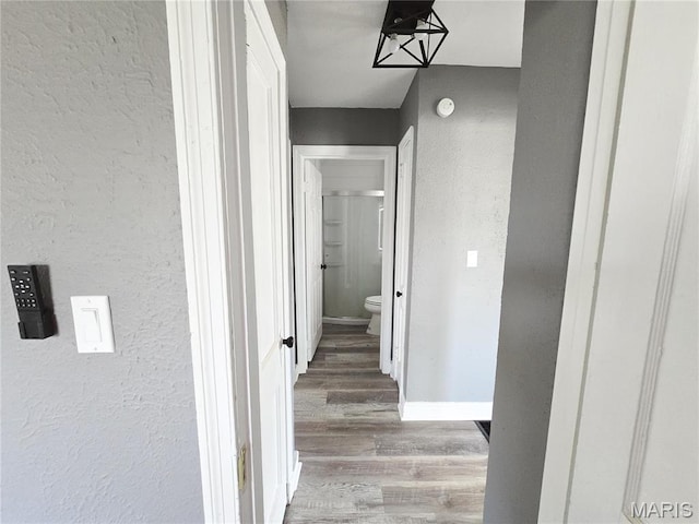 hallway featuring wood finished floors, a textured wall, and baseboards