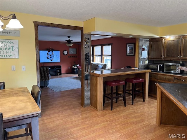 10303 Woodberry Rd, Potosi, MO 63664 - kitchen with light wood-type flooring, dark brown cabinetry, a breakfast bar area, a ceiling fan, and a textured ceiling