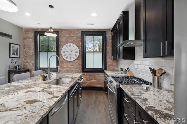 kitchen with stainless steel appliances, wall chimney range hood, a sink, dark wood-type flooring, and light stone countertops