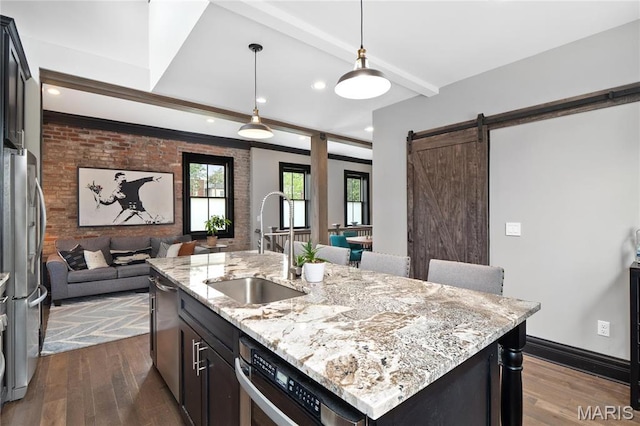 kitchen with a sink, open floor plan, dark wood-style floors, a barn door, and stainless steel appliances