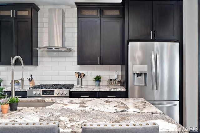 kitchen with appliances with stainless steel finishes, wall chimney range hood, backsplash, and light stone counters