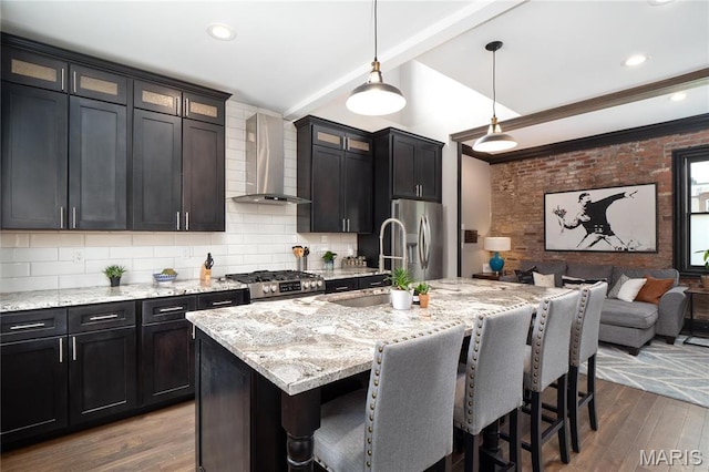 kitchen featuring wall chimney range hood, stainless steel appliances, open floor plan, a sink, and a kitchen bar