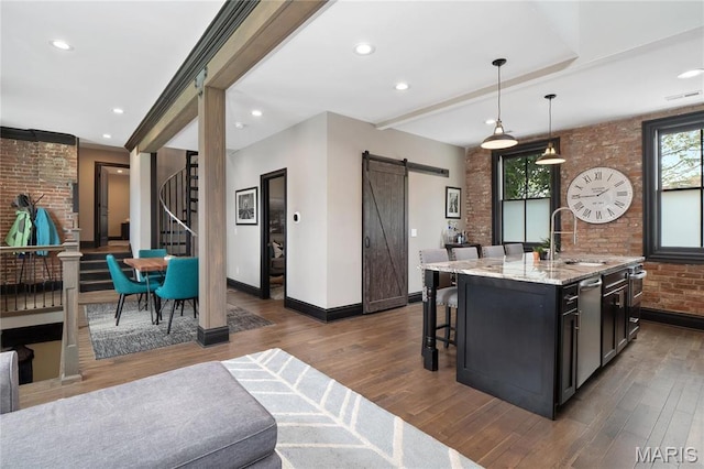 kitchen with a sink, a barn door, baseboards, brick wall, and wood finished floors