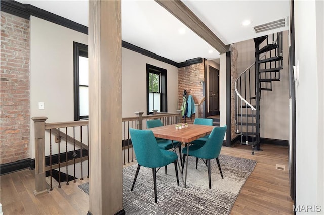 dining area featuring hardwood / wood-style flooring, baseboards, crown molding, stairs, and brick wall