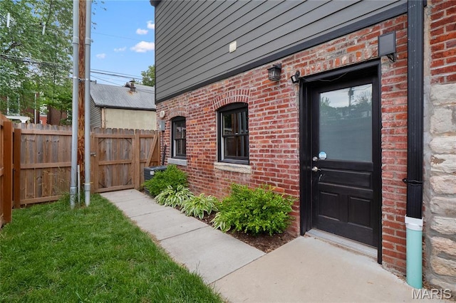 view of exterior entry featuring brick siding and fence
