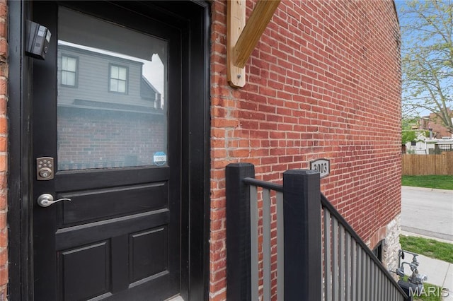 view of exterior entry featuring brick siding and fence