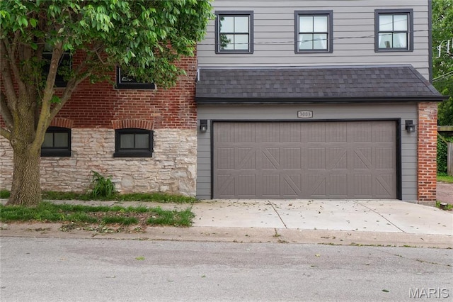 view of front of home with a shingled roof, stone siding, a garage, and brick siding