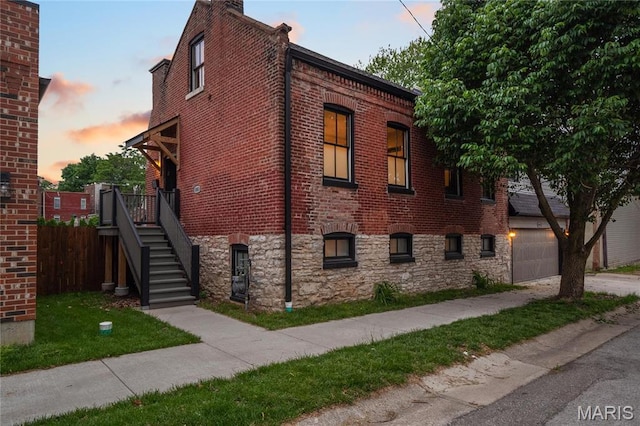 view of side of home with a garage, brick siding, driveway, fence, and stairway