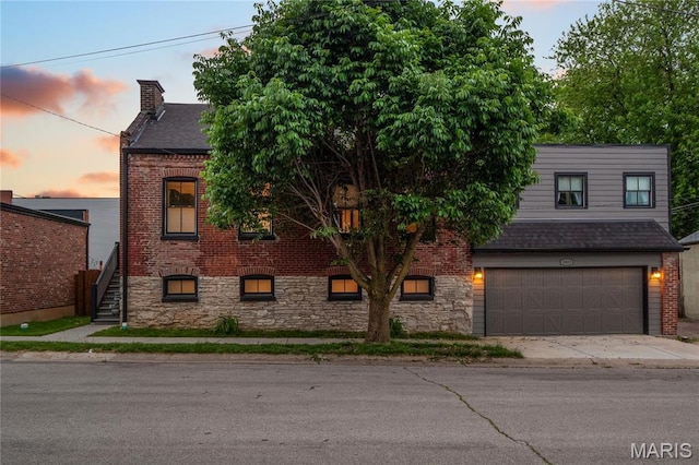view of front of house with brick siding, an attached garage, a chimney, roof with shingles, and driveway