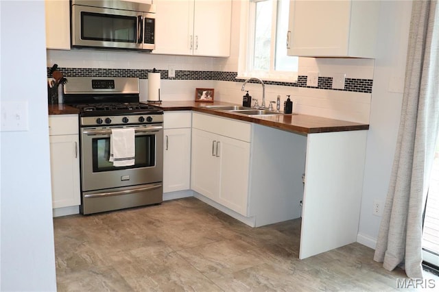 kitchen with stainless steel appliances, a sink, decorative backsplash, butcher block counters, and white cabinetry