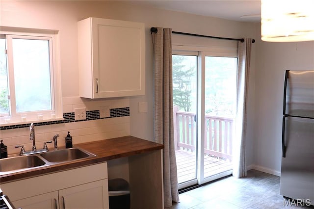 kitchen featuring freestanding refrigerator, a sink, white cabinets, wooden counters, and tasteful backsplash