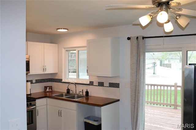 kitchen with a sink, gas stove, wooden counters, decorative backsplash, and white cabinets