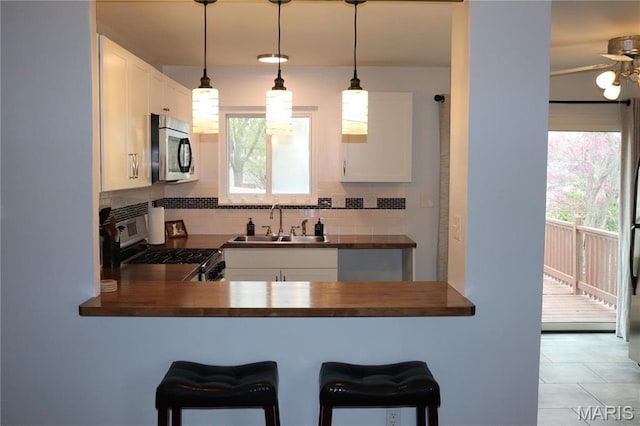 kitchen with appliances with stainless steel finishes, a sink, tasteful backsplash, and butcher block counters