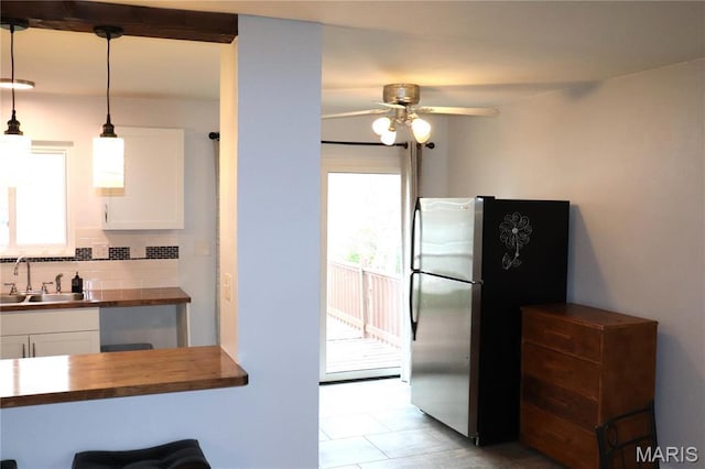 kitchen featuring a sink, wood counters, freestanding refrigerator, a ceiling fan, and white cabinets
