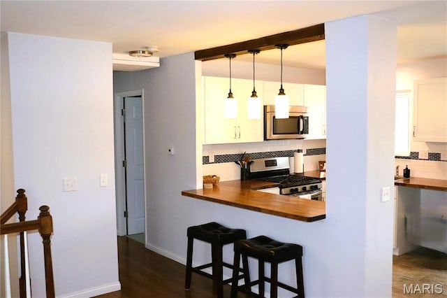 kitchen with stainless steel appliances, butcher block counters, backsplash, a kitchen bar, and white cabinets
