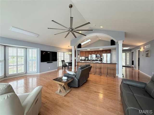 living room featuring ornate columns, a ceiling fan, vaulted ceiling, baseboards, and light wood-style flooring