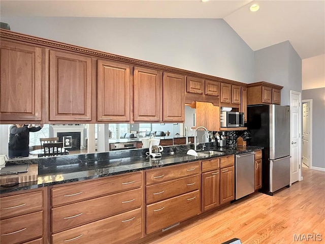 kitchen with stainless steel appliances, high vaulted ceiling, a sink, brown cabinetry, and light wood-type flooring