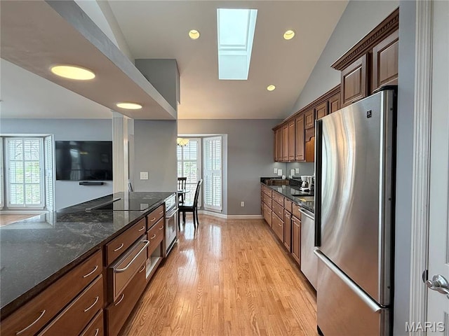kitchen with freestanding refrigerator, a skylight, light wood-style floors, lofted ceiling, and dark stone counters