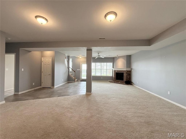 unfurnished living room with carpet flooring, baseboards, a ceiling fan, a brick fireplace, and stairs