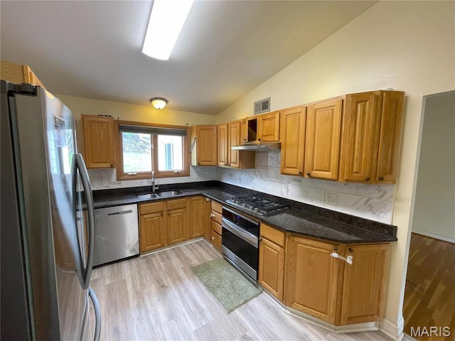 kitchen with stainless steel appliances, a sink, light wood finished floors, lofted ceiling, and decorative backsplash