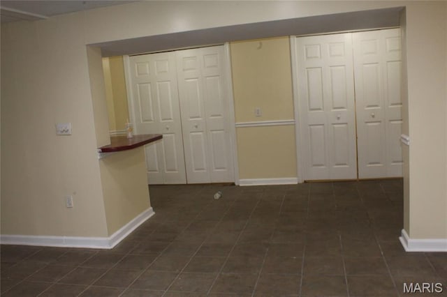 hallway featuring baseboards and dark tile patterned floors