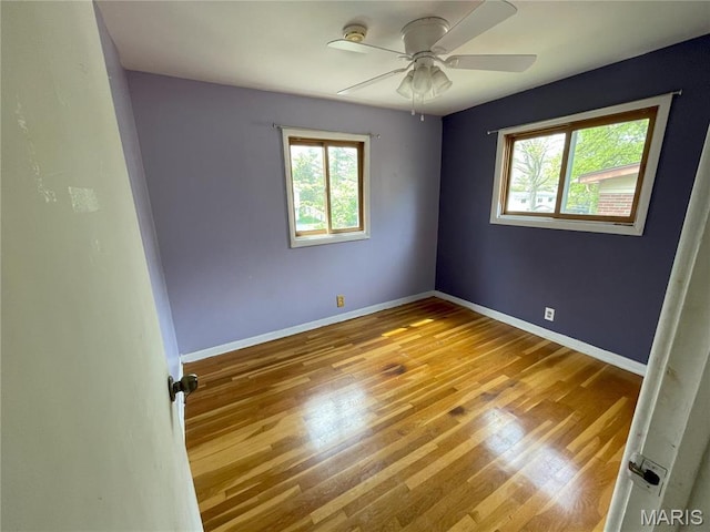 spare room with healthy amount of natural light, ceiling fan, wood finished floors, and baseboards