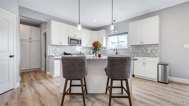 kitchen with stainless steel microwave, a breakfast bar area, white cabinetry, and recessed lighting