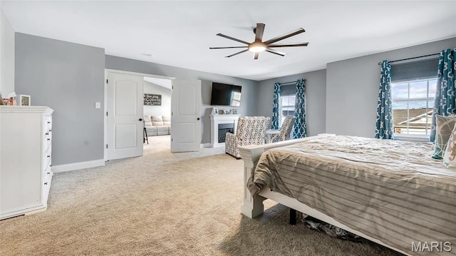 bedroom with carpet, a glass covered fireplace, baseboards, and a ceiling fan