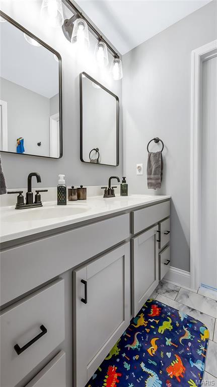 bathroom featuring marble finish flooring, double vanity, and baseboards