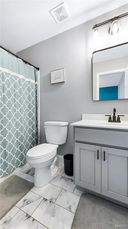 full bath featuring marble look tiles, toilet, vanity, and curtained shower