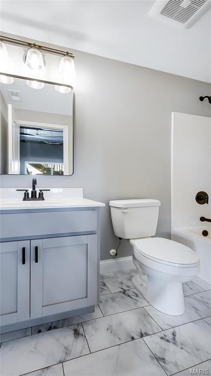 bathroom featuring marble finish floors, toilet, vanity, and washtub / shower combination