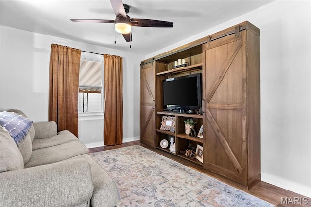 living room featuring a barn door, baseboards, ceiling fan, and wood finished floors