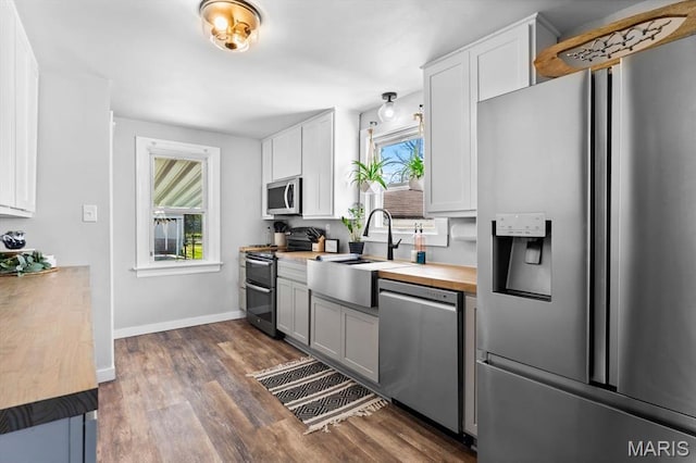 kitchen featuring appliances with stainless steel finishes, wooden counters, a sink, dark wood finished floors, and white cabinets