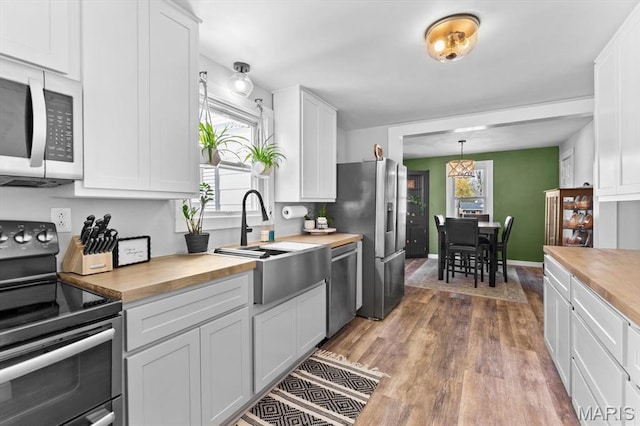 kitchen with appliances with stainless steel finishes, wooden counters, wood finished floors, and white cabinets