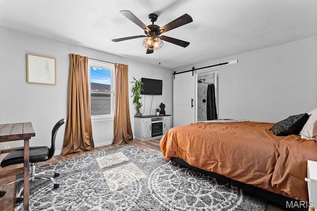 bedroom featuring a barn door, wood finished floors, a ceiling fan, and baseboards