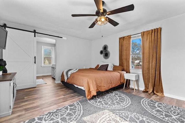 bedroom with a barn door, baseboards, wood finished floors, and ceiling fan