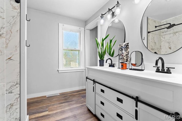 bathroom with a marble finish shower, wood finished floors, double vanity, and baseboards