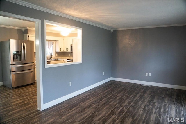 spare room featuring dark wood-type flooring, a sink, ornamental molding, and baseboards