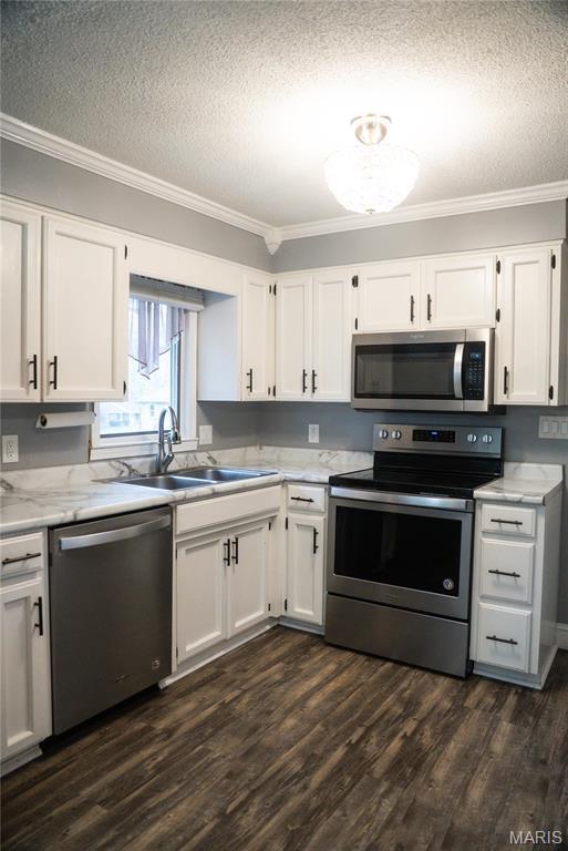 kitchen featuring stainless steel appliances, ornamental molding, a textured ceiling, a sink, and white cabinets