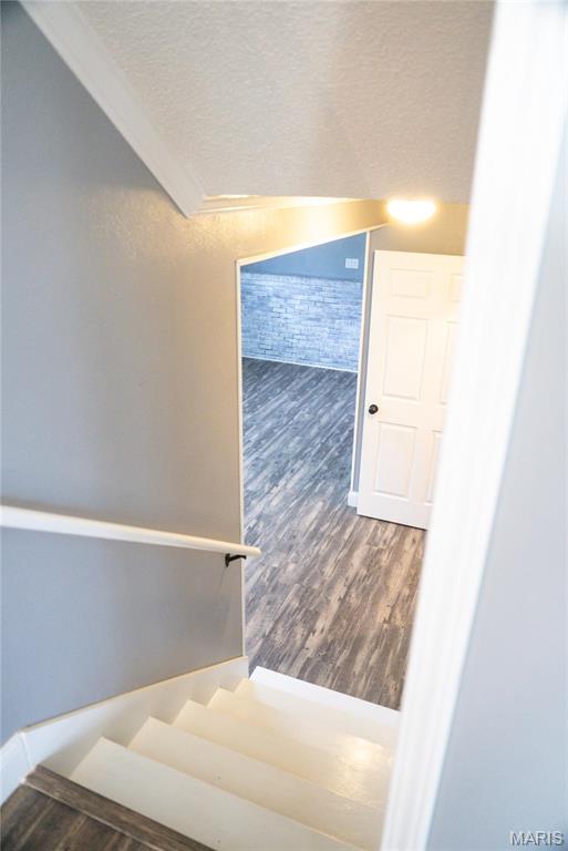 staircase with wood finished floors, lofted ceiling, and a textured ceiling