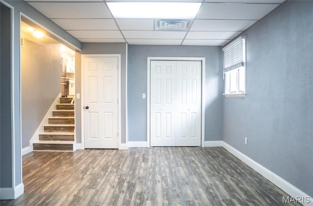 unfurnished bedroom with a drop ceiling, wood finished floors, a closet, and baseboards