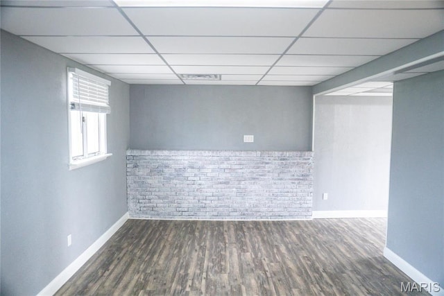 below grade area featuring a paneled ceiling, brick wall, wood finished floors, and baseboards
