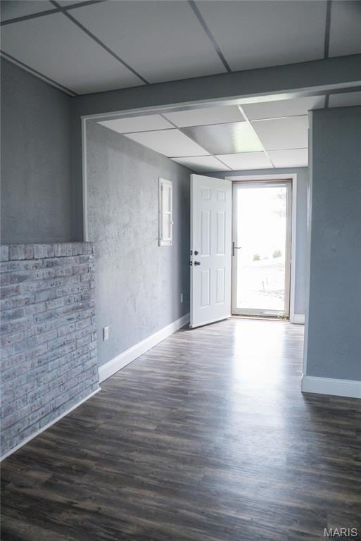 empty room featuring wood finished floors, baseboards, and a paneled ceiling