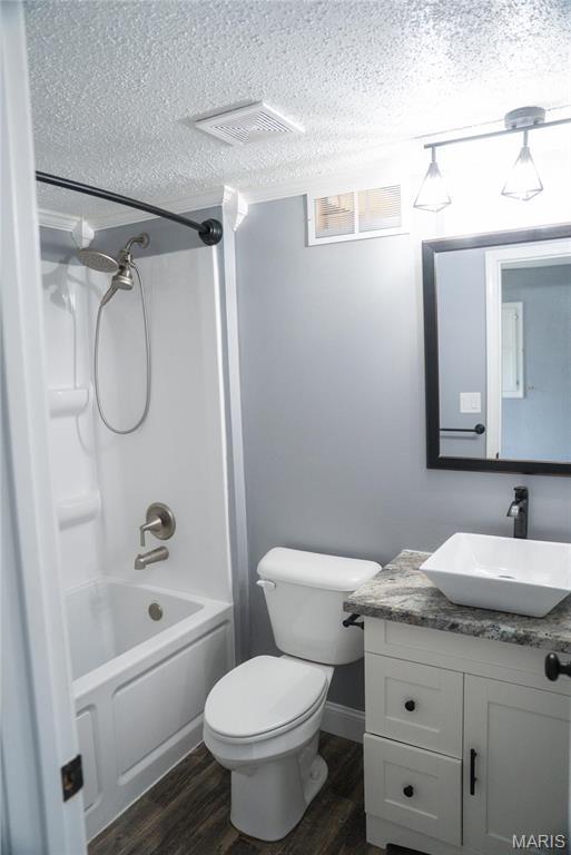 full bathroom with wood finished floors, a textured ceiling, vanity, toilet, and bathtub / shower combination
