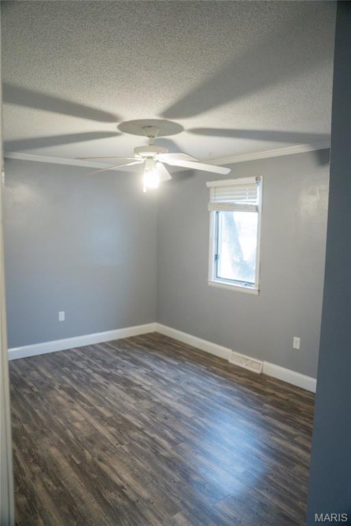 empty room featuring a textured ceiling, a ceiling fan, crown molding, dark wood finished floors, and baseboards