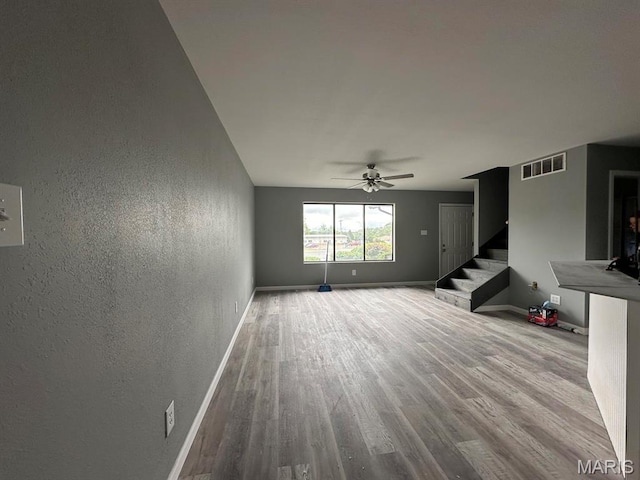unfurnished living room with stairs, wood finished floors, a textured wall, baseboards, and ceiling fan