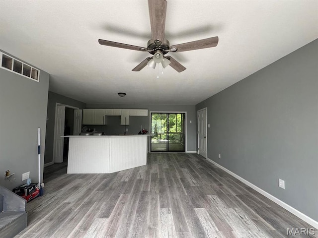 unfurnished living room featuring ceiling fan, wood finished floors, and baseboards