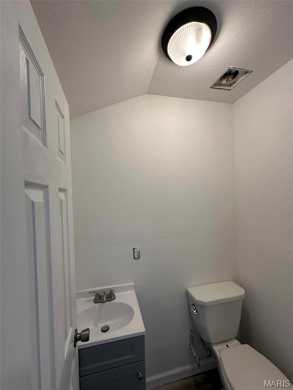 half bathroom featuring toilet, vanity, lofted ceiling, and baseboards